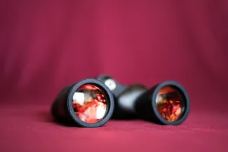 a pair of binoculars sitting on top of a red cloth by Kelli McClintock courtesy of Unsplash.